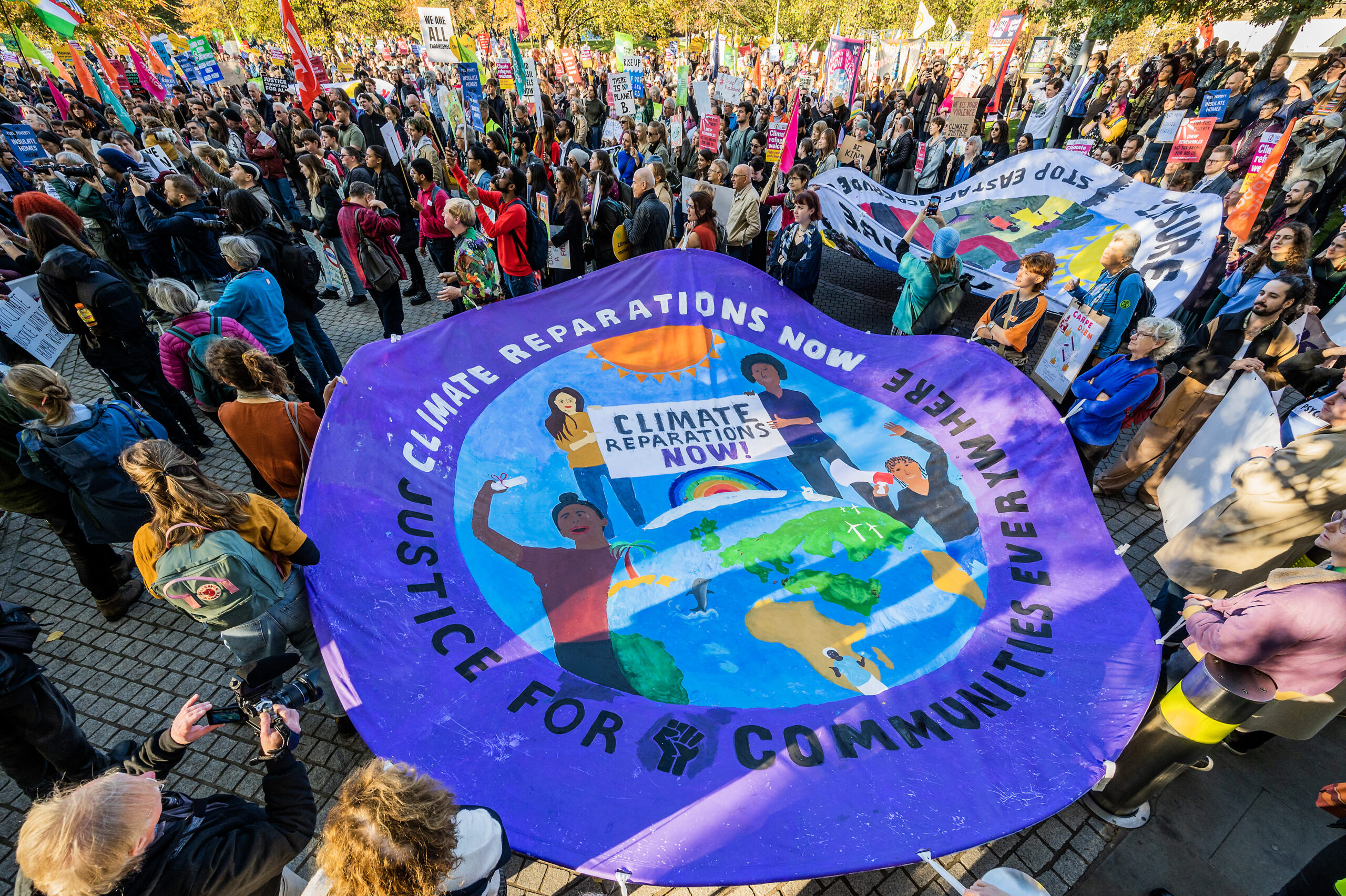 People hold a giant circulate banner calling for climate reparations